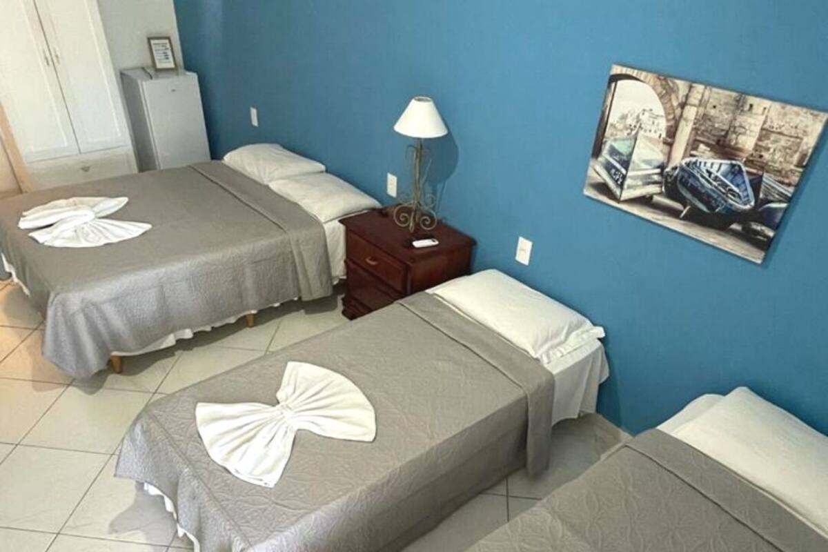 A hotel room with two beds, each with a towel on the bedspread. There is a nightstand with a lamp, a picture on the wall, and a small table with a remote control.