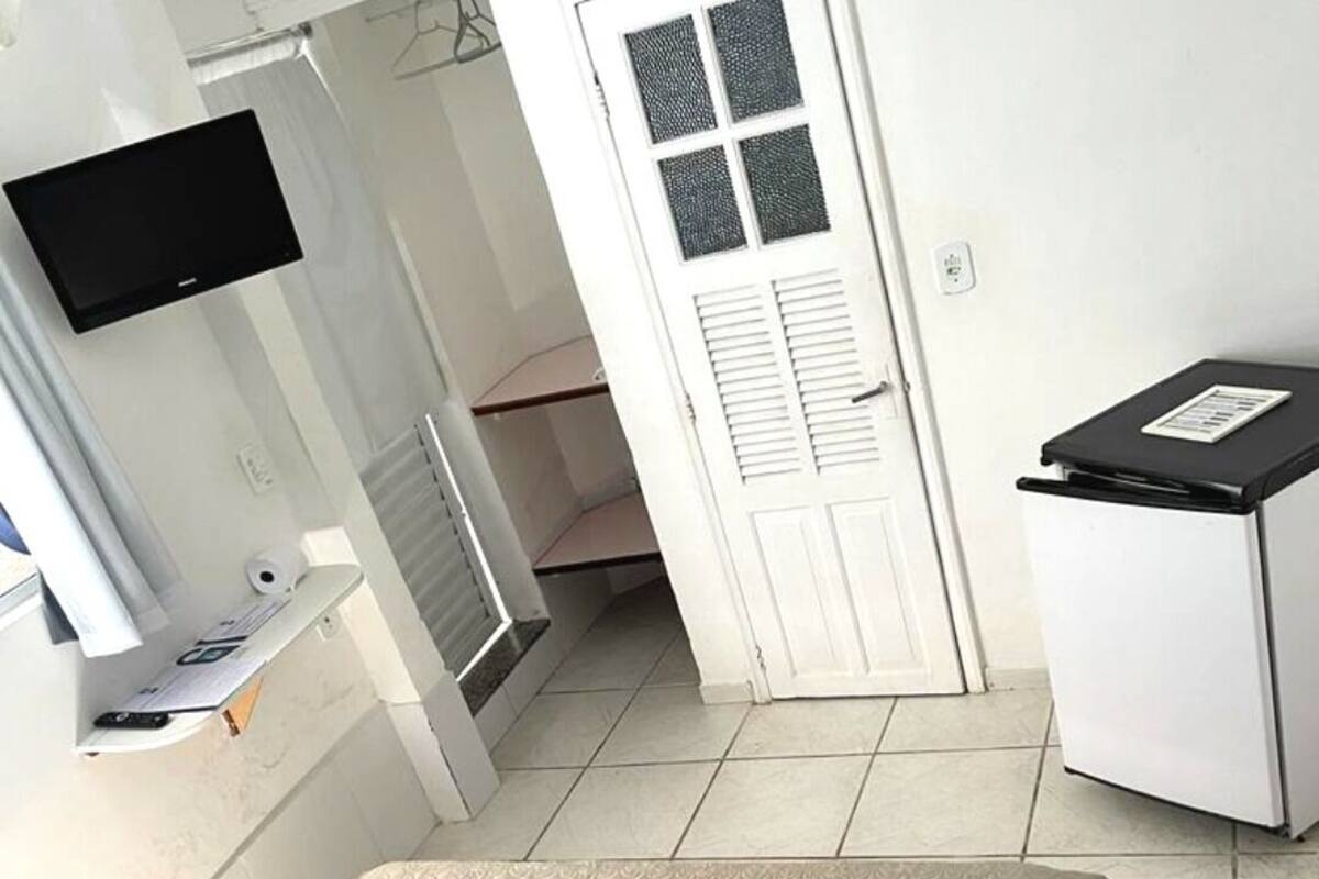 A hotel room with a bed, a TV mounted on the wall, a small desk with a computer, and a door leading to a bathroom.