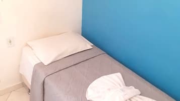 Una cama individual con colcha gris y almohadas blancas, un cuadro de pájaros en la pared y una pared de acento azul.
