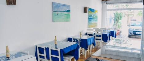 A dining area with tables and chairs, a ceiling fan, and artwork on the walls.