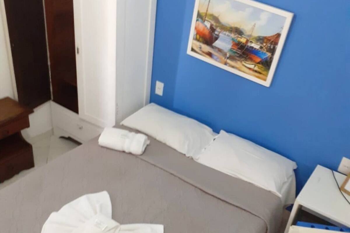 A hotel room with a bed, a painting on the wall, a nightstand, and a suitcase.