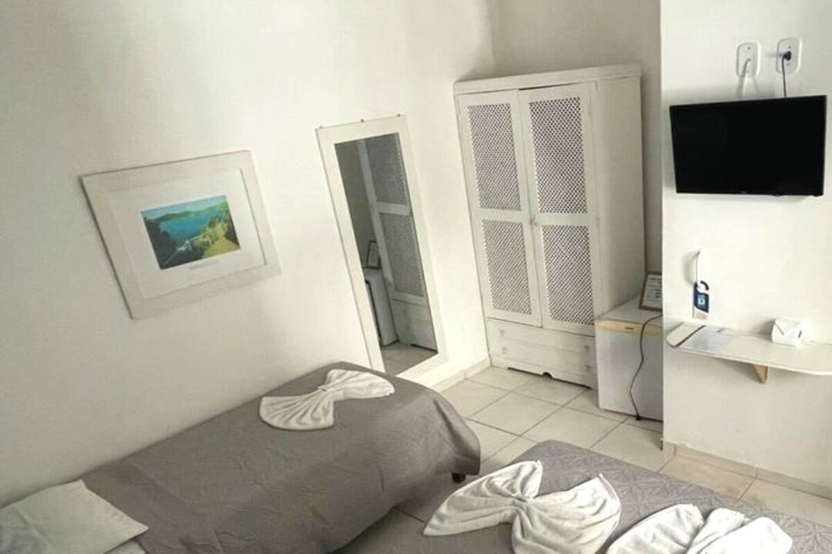 A hotel room with two beds, a wardrobe, a desk, and a TV.