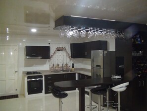 A modern kitchen with a central island, bar stools, a refrigerator, and a wine rack.
