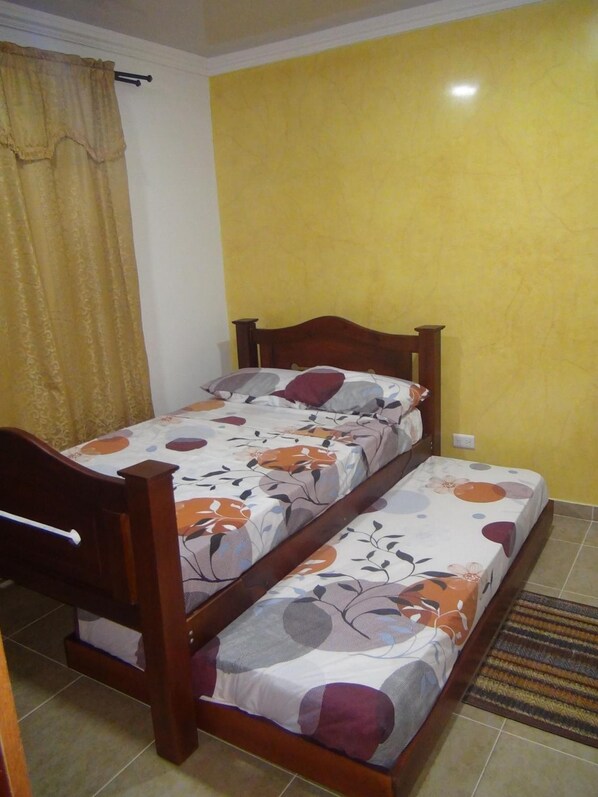 A double bed with floral bedding, a wooden headboard, and a yellow wall.