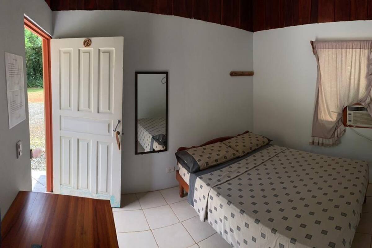 A bedroom with a bed, a door, a mirror, and a window with curtains.
