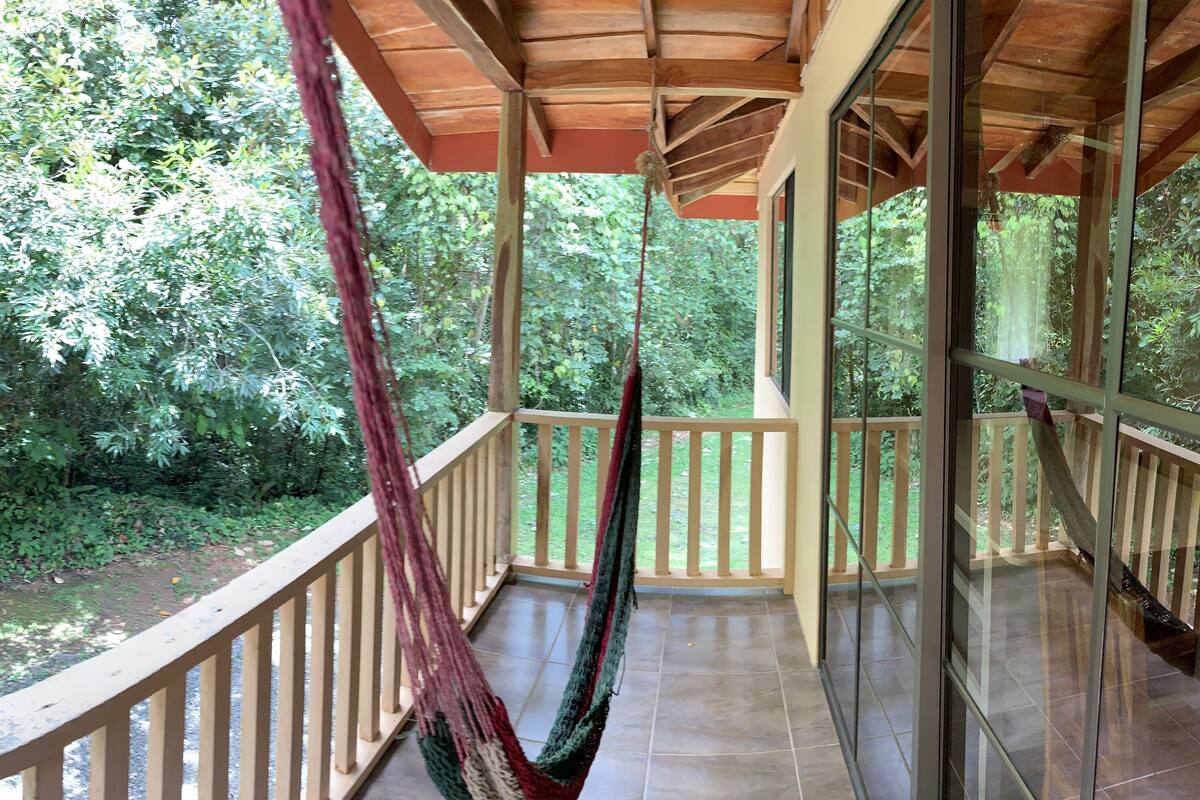 A balcony with a hammock, surrounded by lush greenery and a view of a natural landscape.