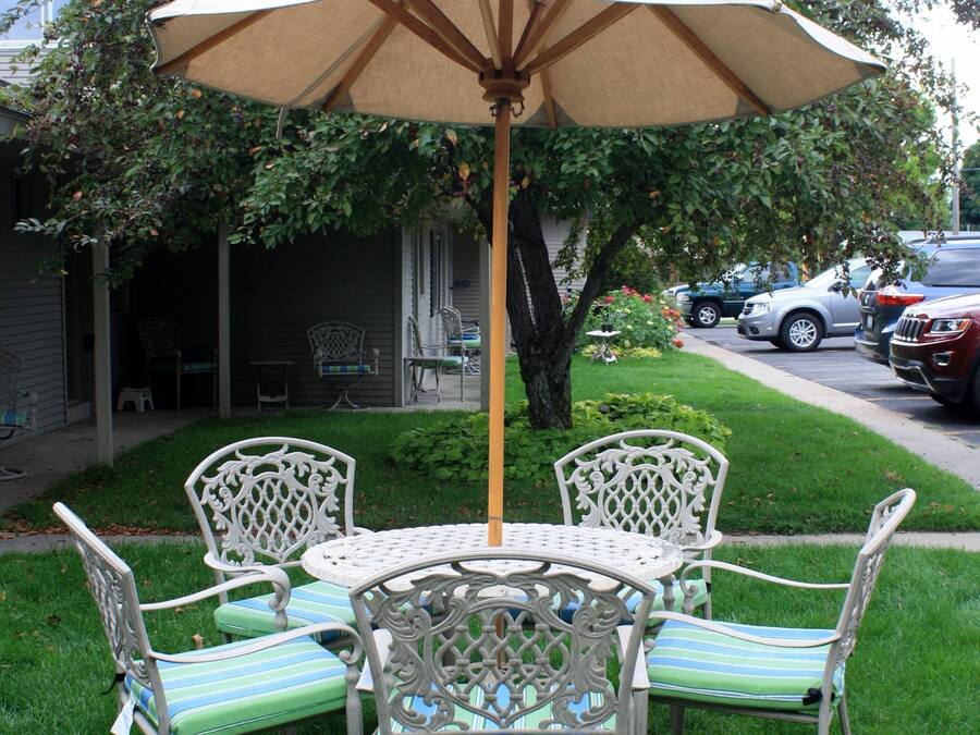 A patio with a table and chairs, an umbrella, and a lawn.