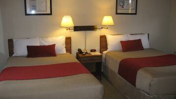 Dos camas matrimoniales con almohadones rojos, una mesita de noche con teléfono y despertador, y dos lámparas de pared.