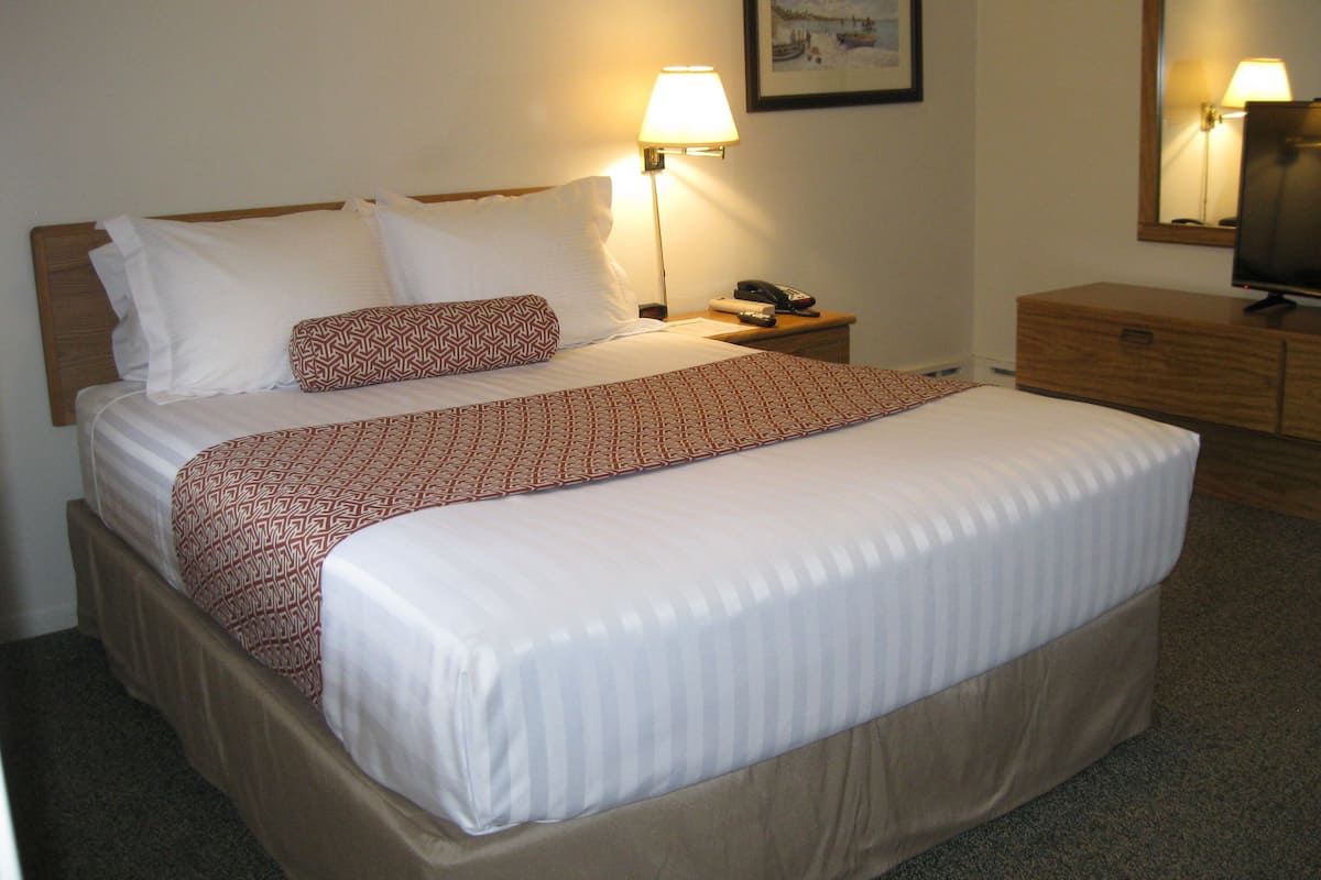 A hotel room with a large bed, a bedside table with a lamp, a TV, and a wooden nightstand.