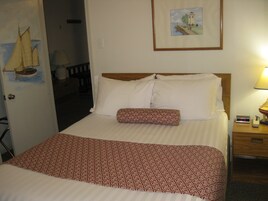 A hotel room with a bed, a nightstand with a lamp, a framed picture on the wall, and a door with a sailboat illustration.