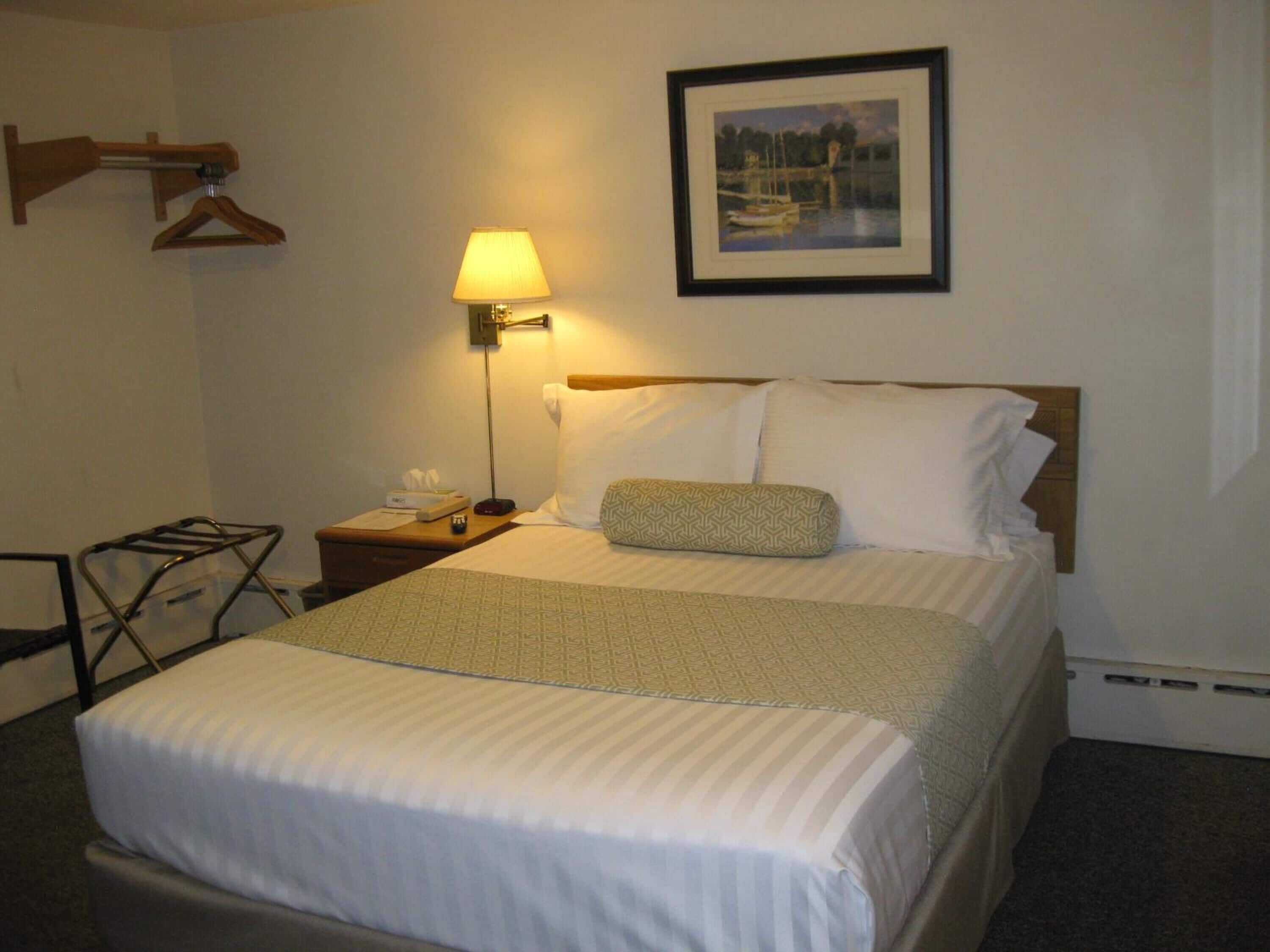 A hotel room with a bed, a bedside lamp, a framed picture on the wall, and a small table with a telephone and tissues.