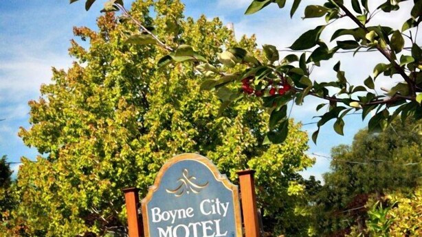 A motel sign with the name "Boyne City Motel" surrounded by lush greenery and flowers. - Boyne City Motel (Boyne City)