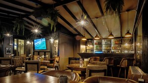 Eine Bar mit Holztischen und -stühlen, einem Fernsehbildschirm und einer Theke voller Flaschen.