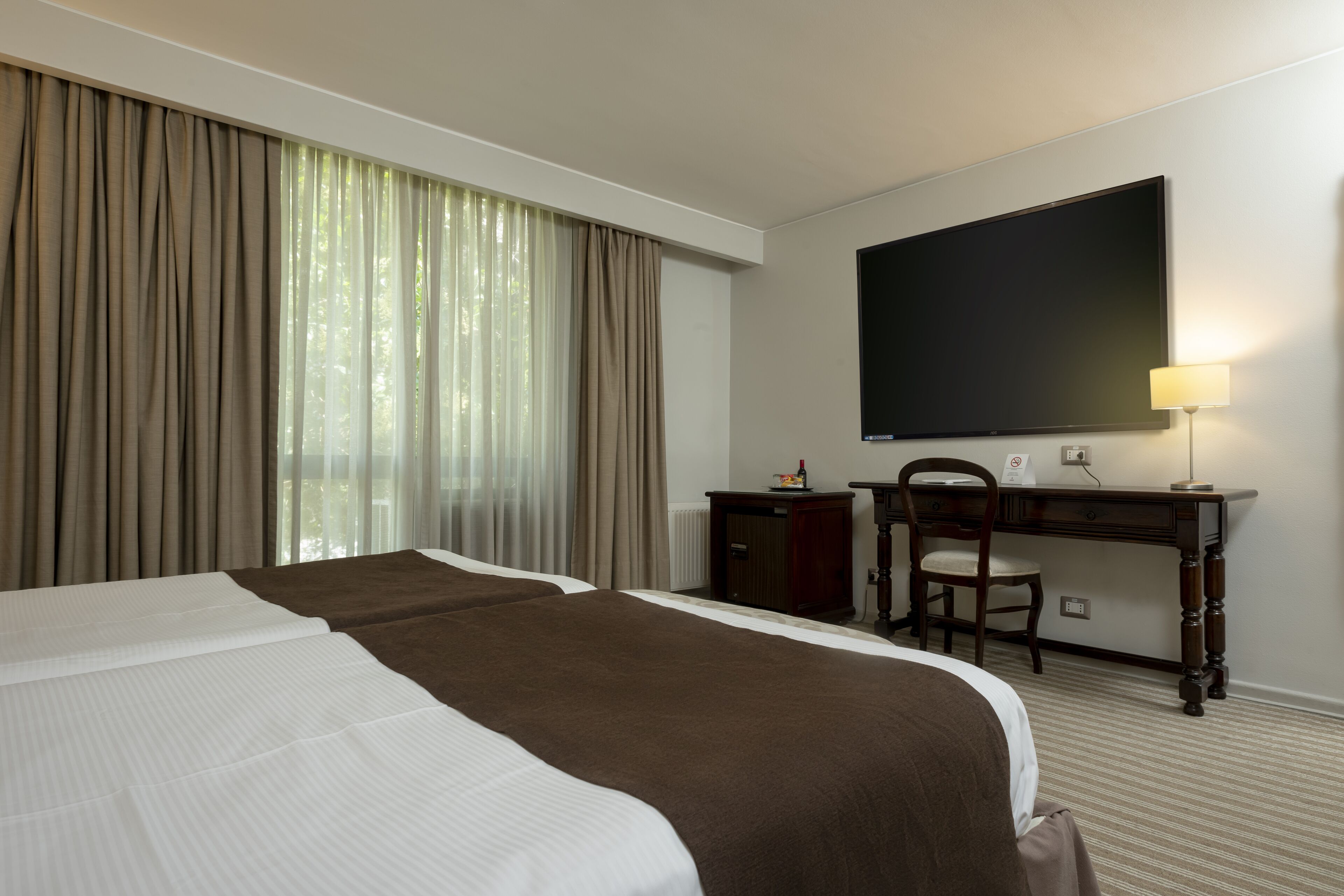 A hotel room with a large bed, a desk, a chair, a flat-screen TV, and a window with curtains.
