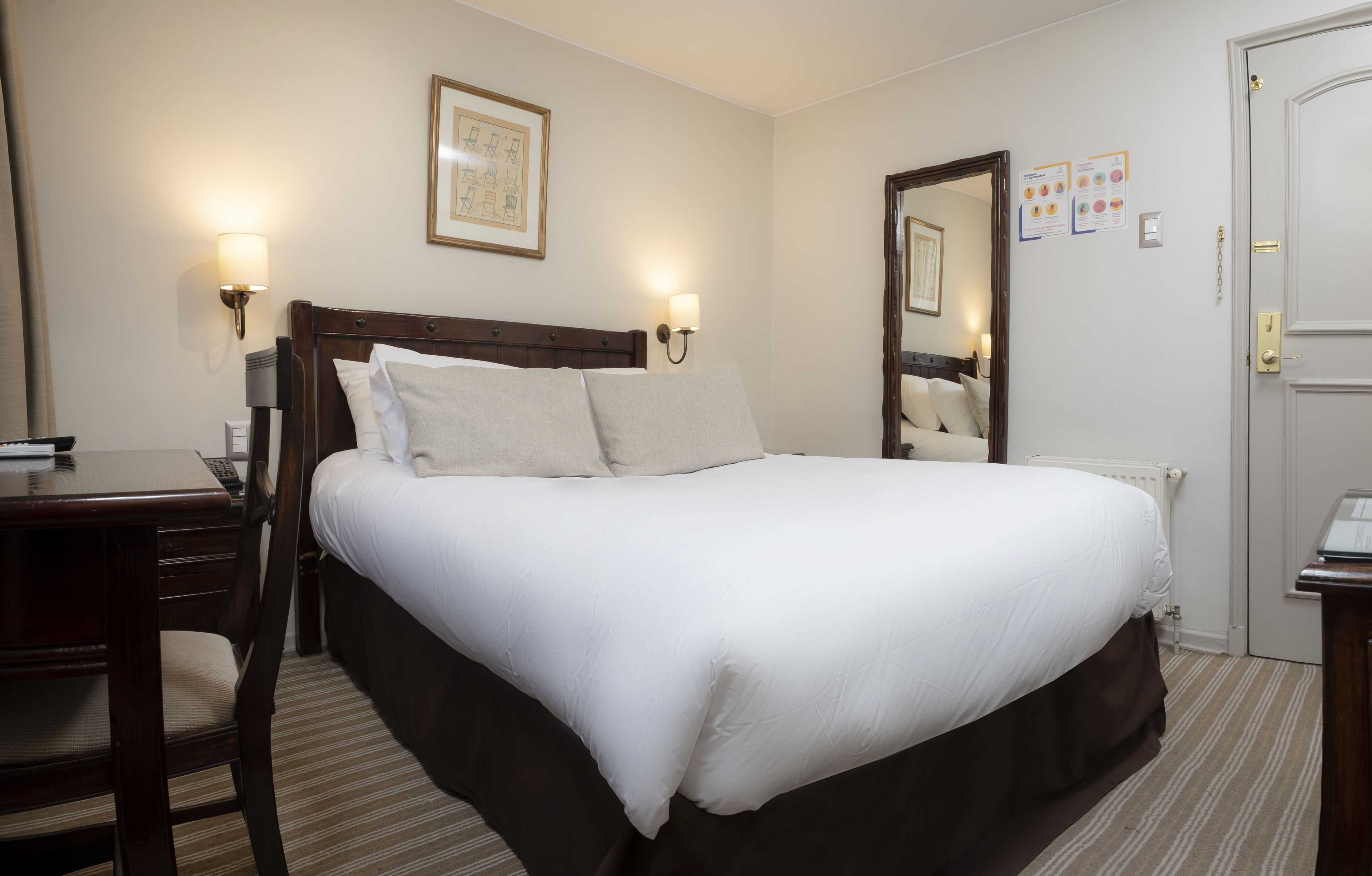 A hotel room with a large bed, bedside lamps, a wooden nightstand, a desk, and a chair.