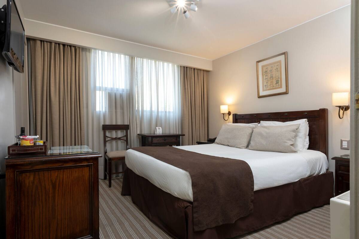 Ein Hotelzimmer mit Bett, Schreibtisch, Sessel, Fernseher und einem Fenster mit Vorhängen.