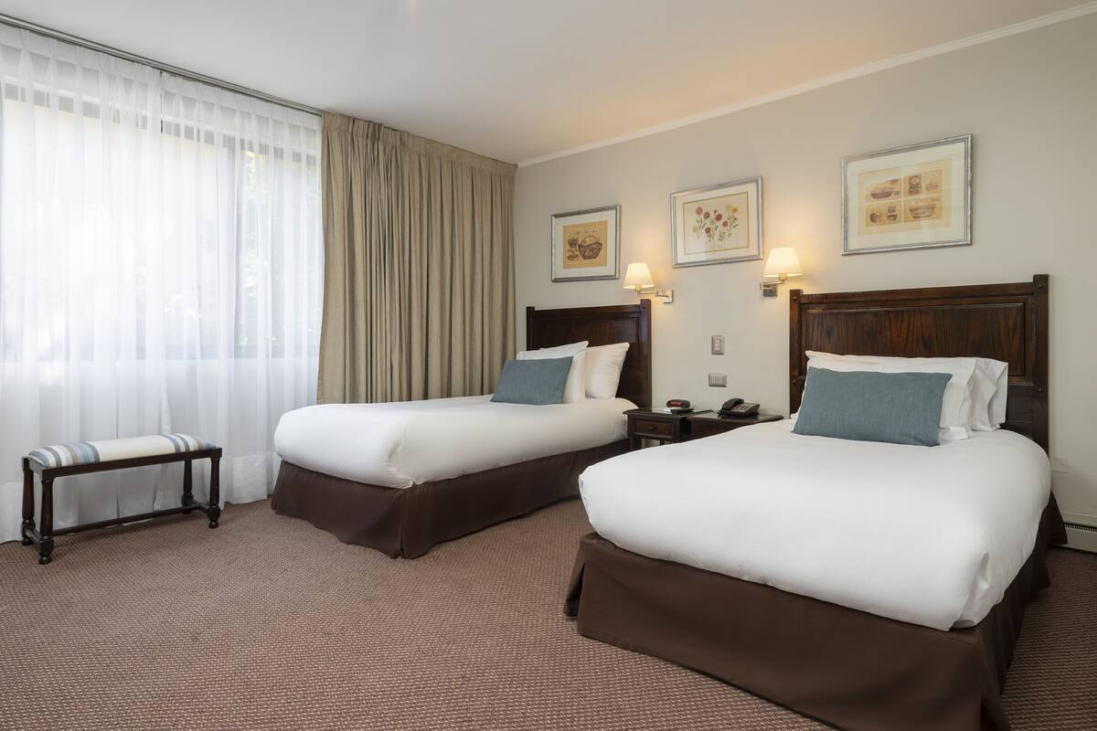 Ein Hotelzimmer mit zwei Betten, einer Bank und einem Fenster mit Vorhängen.