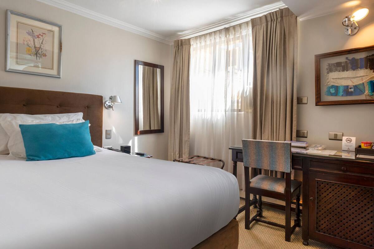 Ein Hotelzimmer mit einem großen Bett, einem Schreibtisch mit Stuhl, einem Spiegel und einem gerahmten Bild an der Wand.