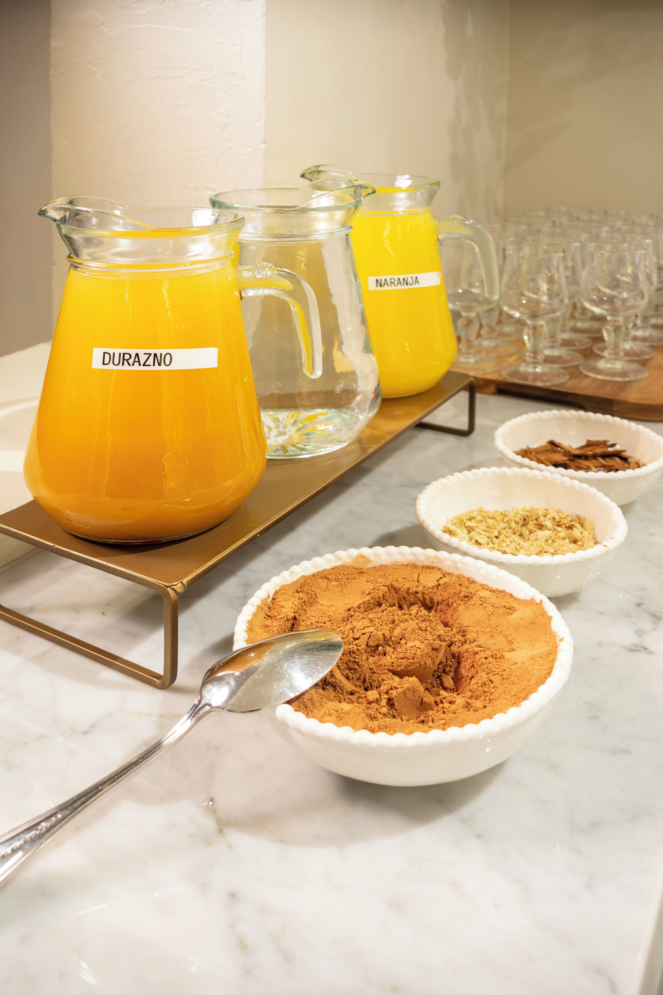 Ein Getränkeausgabe mit beschrifteten Kännchen Orangensaft und einem Löffel braunen Pulvers.