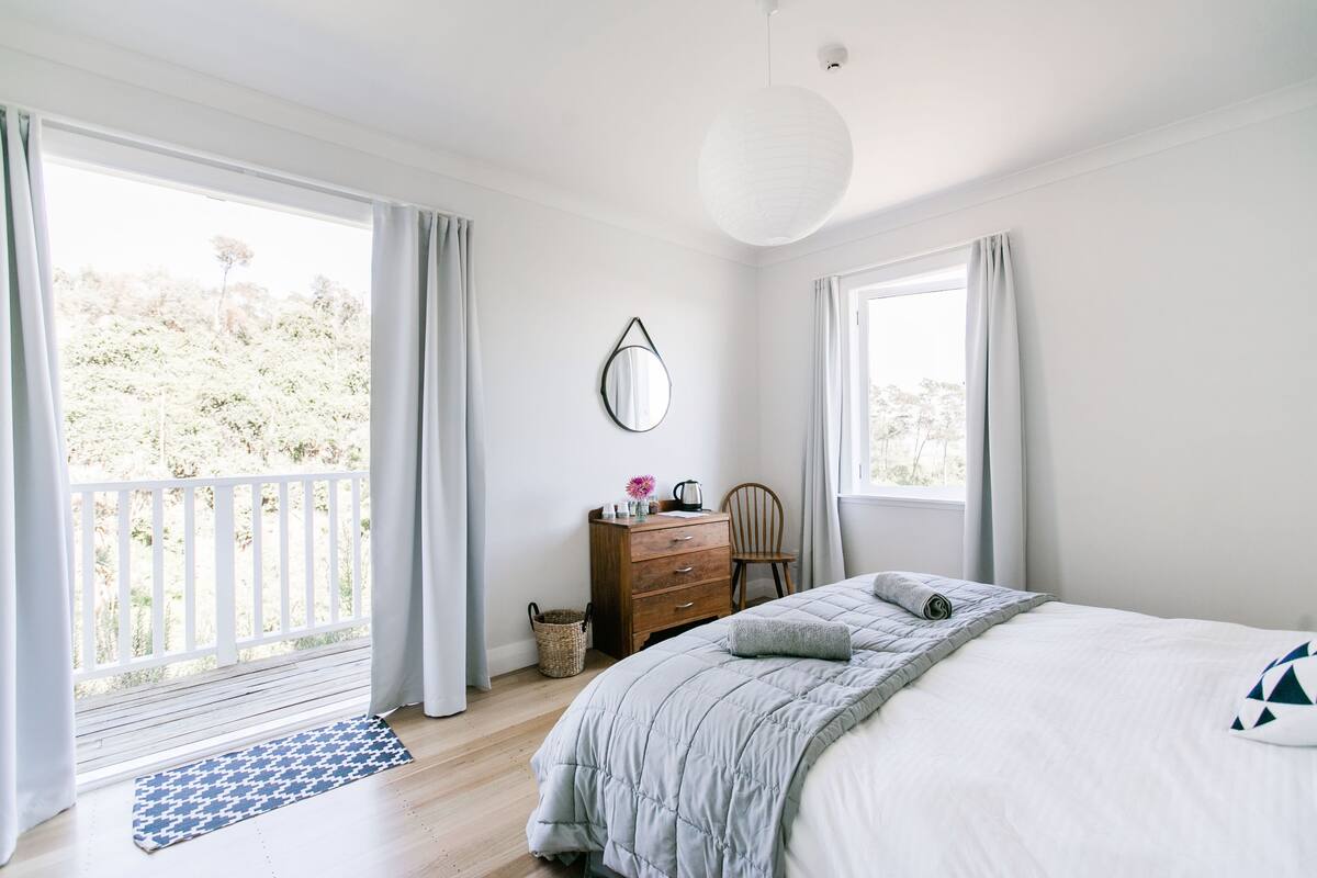 A bedroom with a bed, dresser, chair, and a large window with curtains.