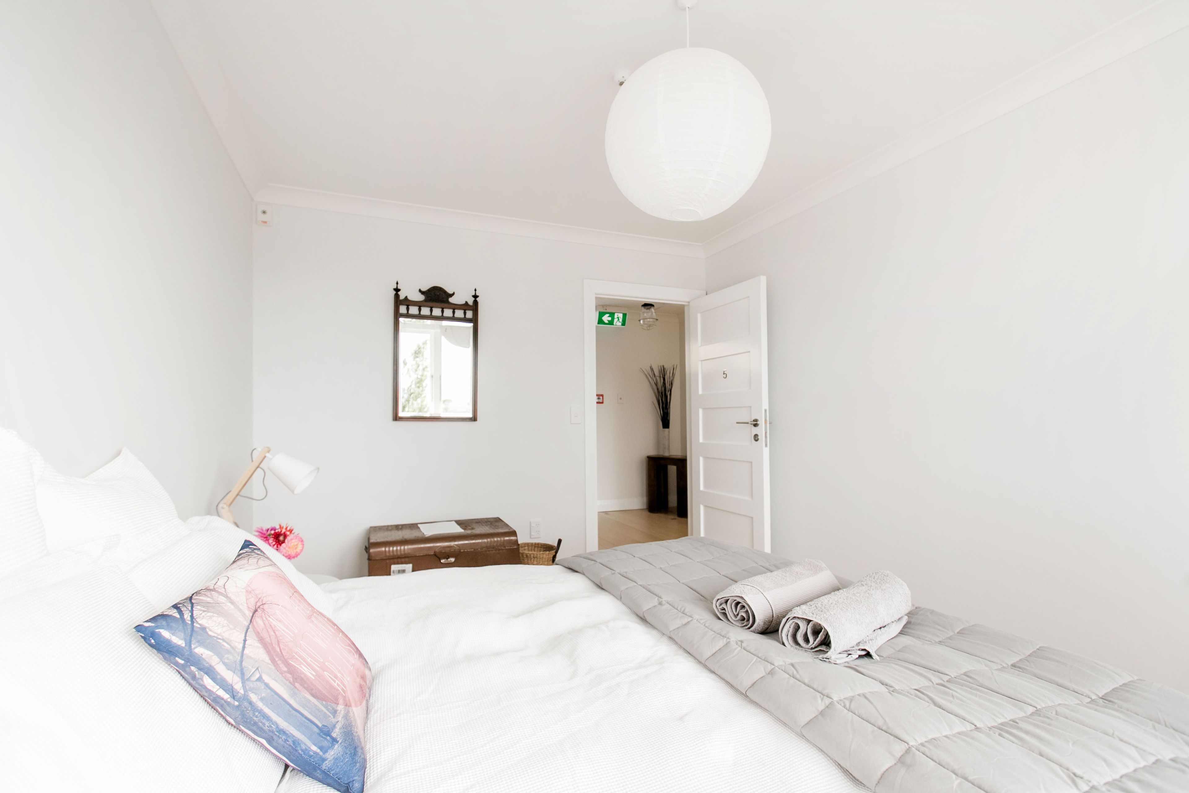 A minimalist bedroom with a bed, a bedside table, a lamp, and a door leading to another room.