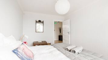 A minimalist bedroom with a bed, a bedside table, a lamp, and a door leading to another room.