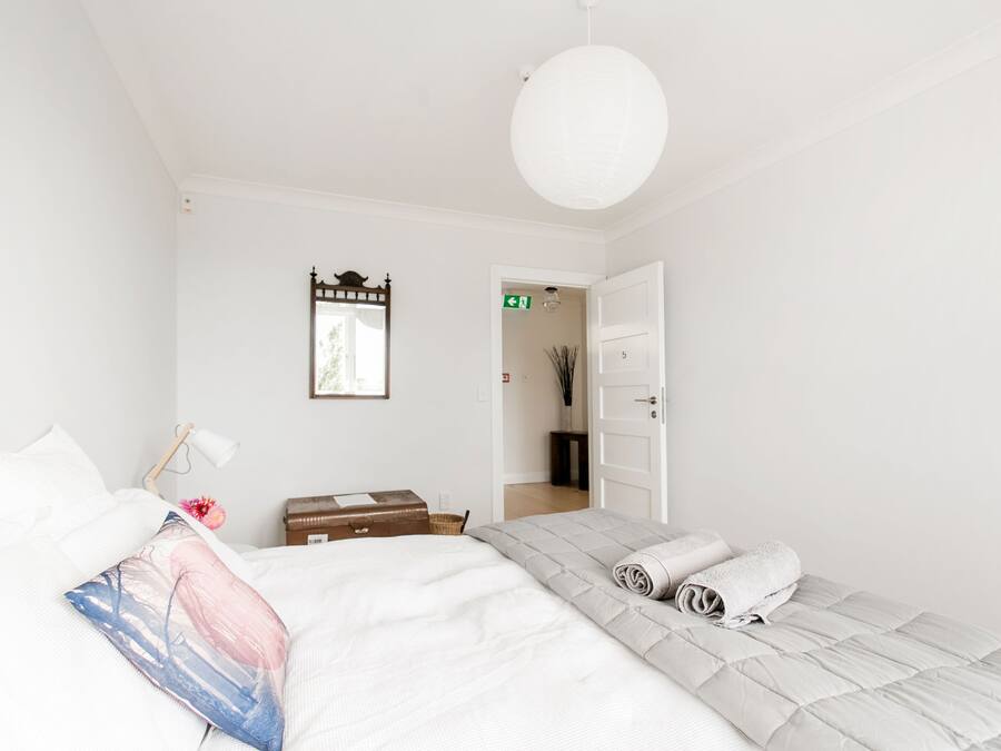 A minimalist bedroom with a bed, a bedside table, a lamp, and a door leading to another room.