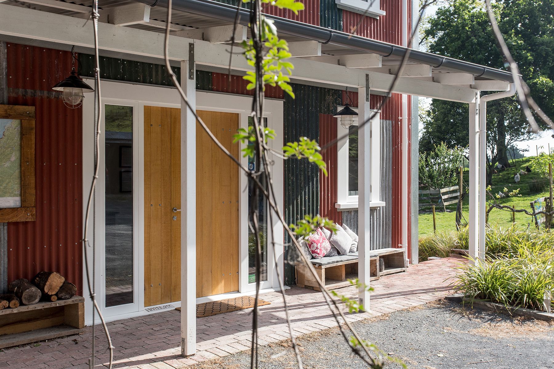 A building with a wooden door, a bench with cushions, and a covered porch area.