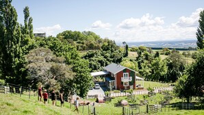 Una casa con balcón, rodeada por un jardín cercado con diversas plantas y una vista despejada del paisaje.