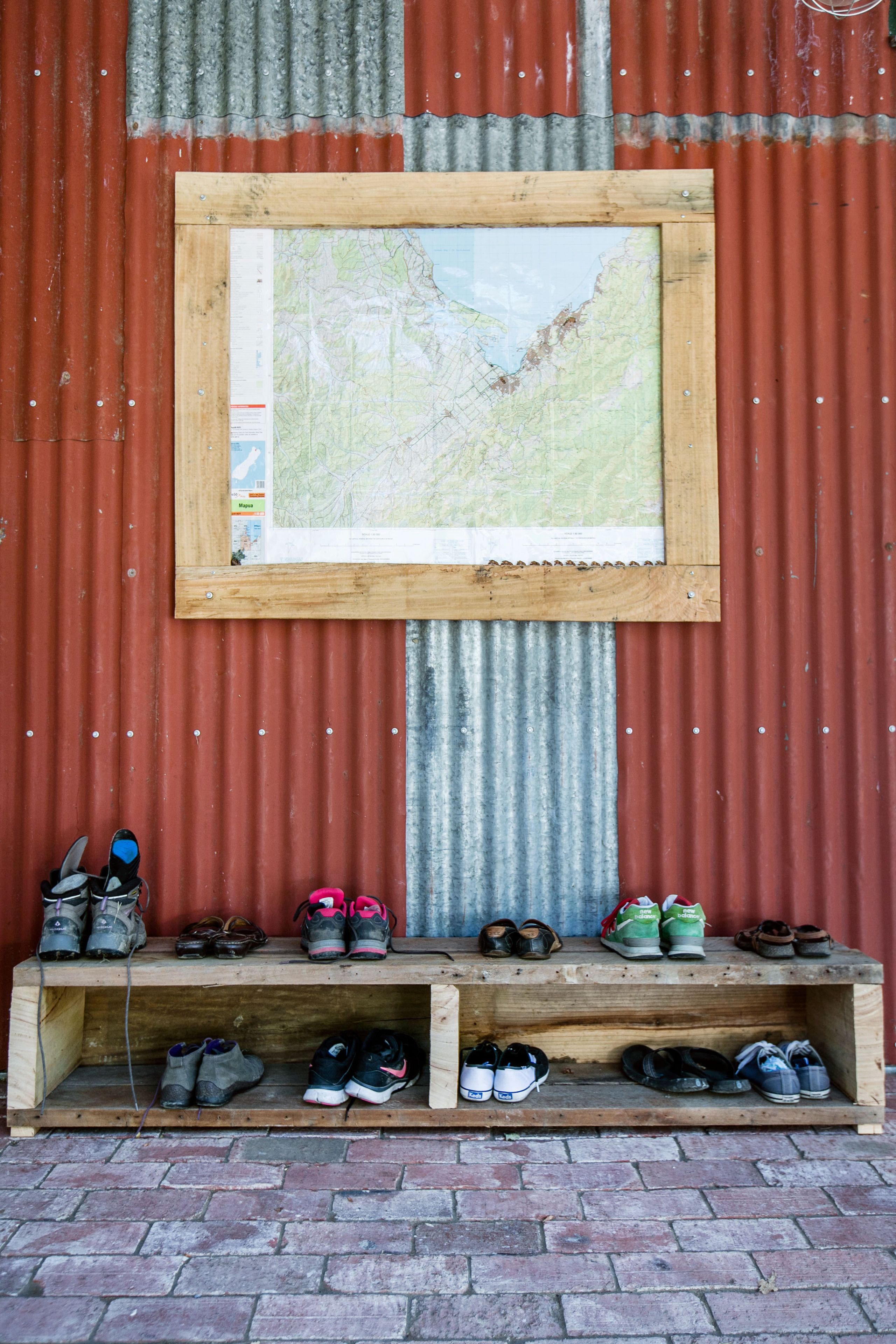 Una mensola di legno con scarpe addossata a un muro in lamiera ondulata.