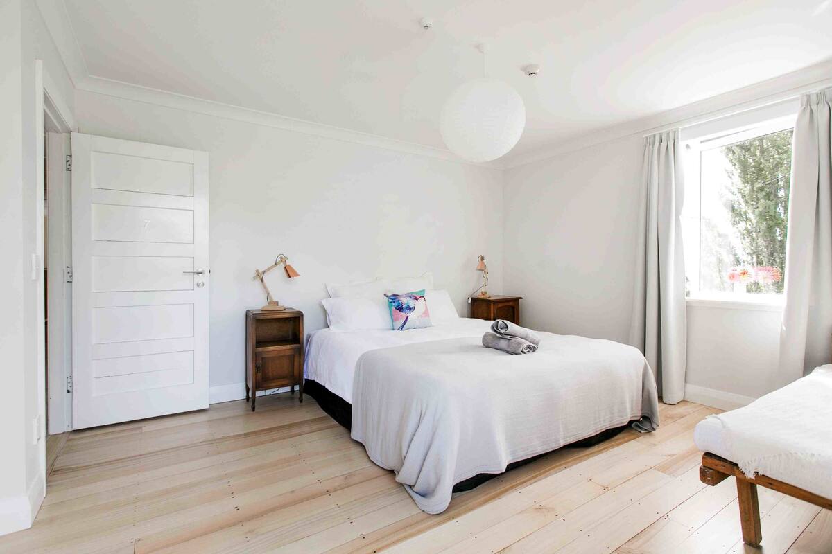 A bedroom with two beds, a white door, and a large window with curtains.