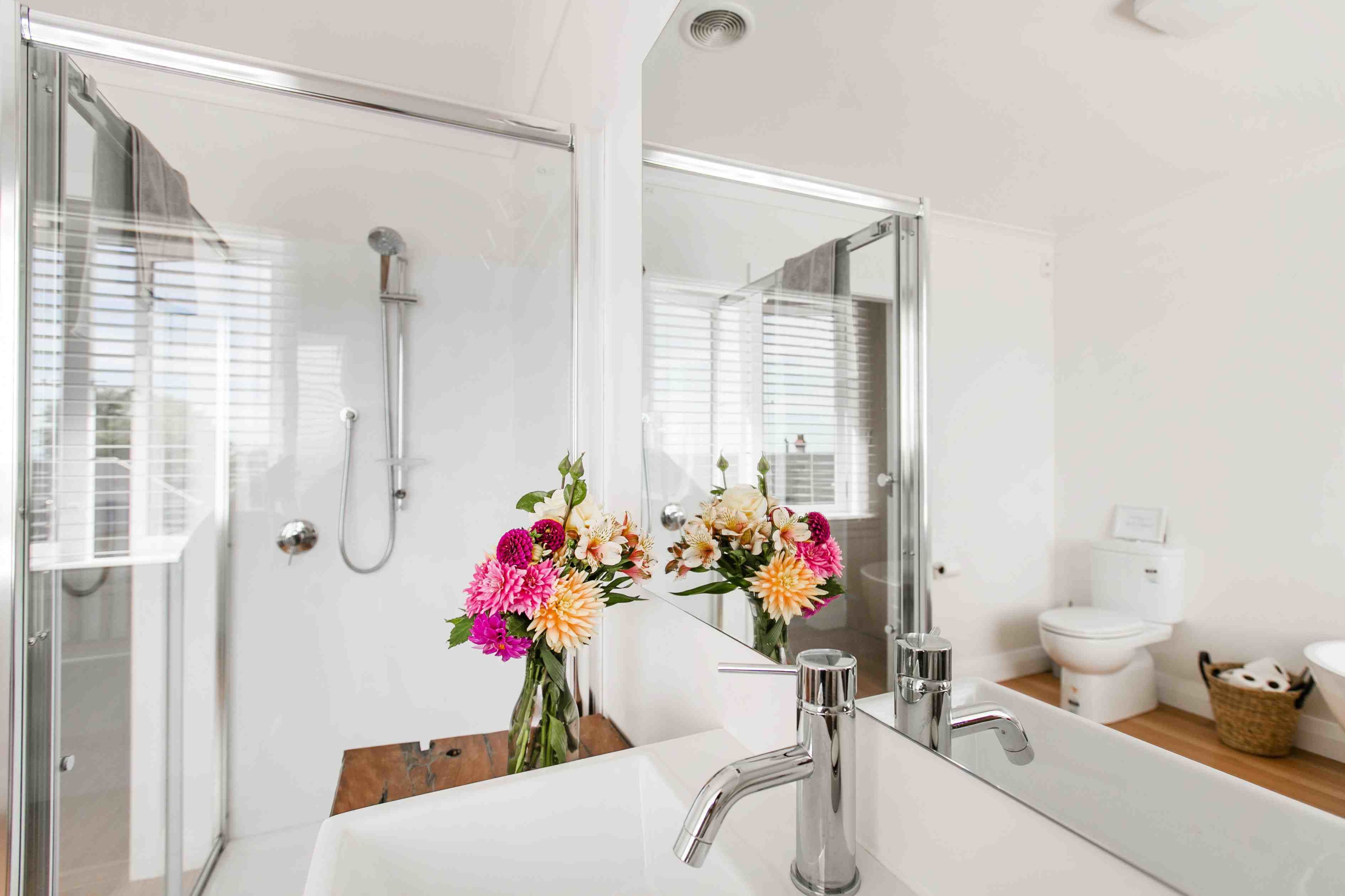 A modern bathroom with a glass shower enclosure, a large mirror, and a white sink with a chrome faucet.