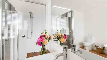 A modern bathroom with a glass shower enclosure, a large mirror, and a white sink with a chrome faucet.