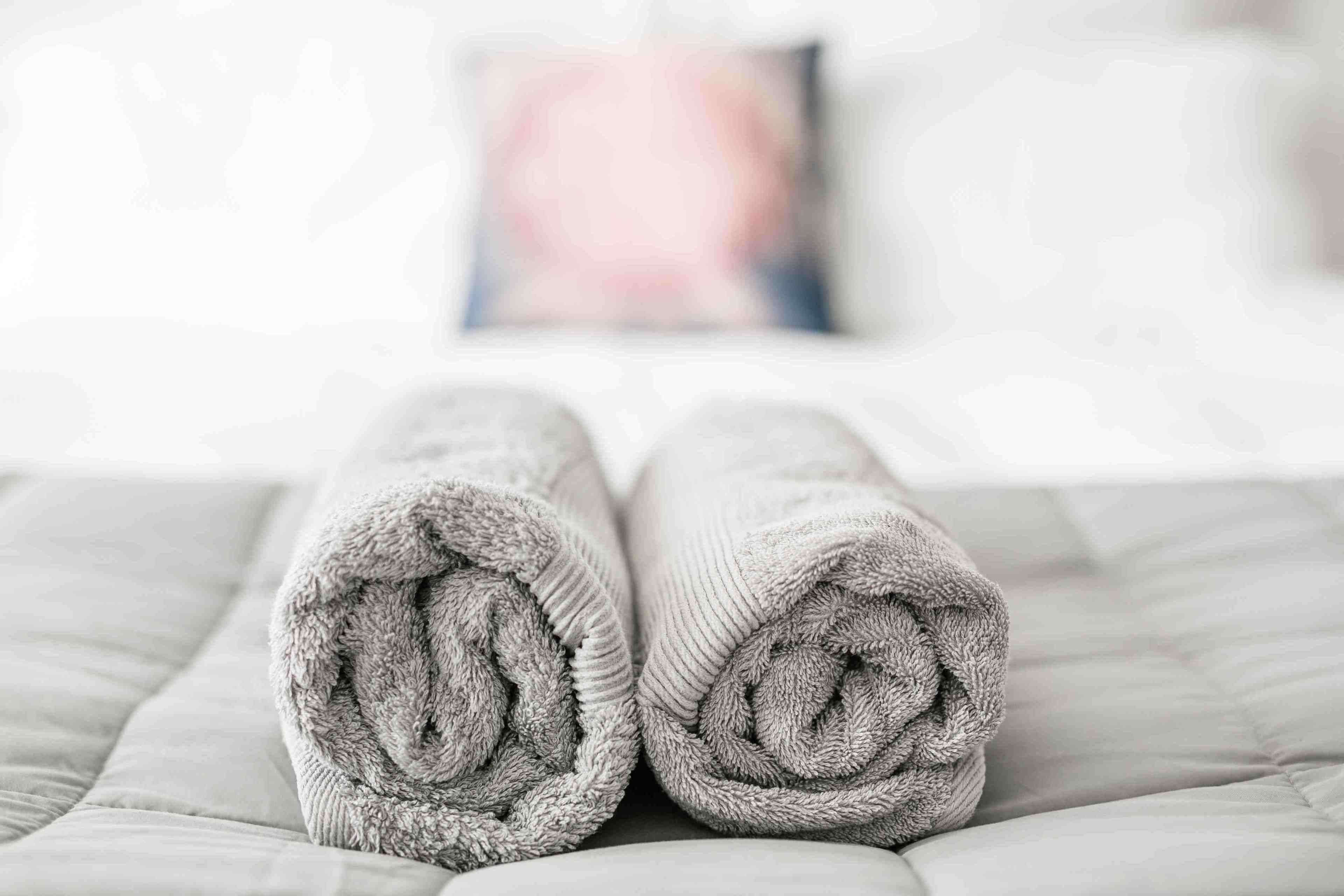 Uma cama com uma toalha cinza bem dobrada e um travesseiro com padrão rosa e azul.