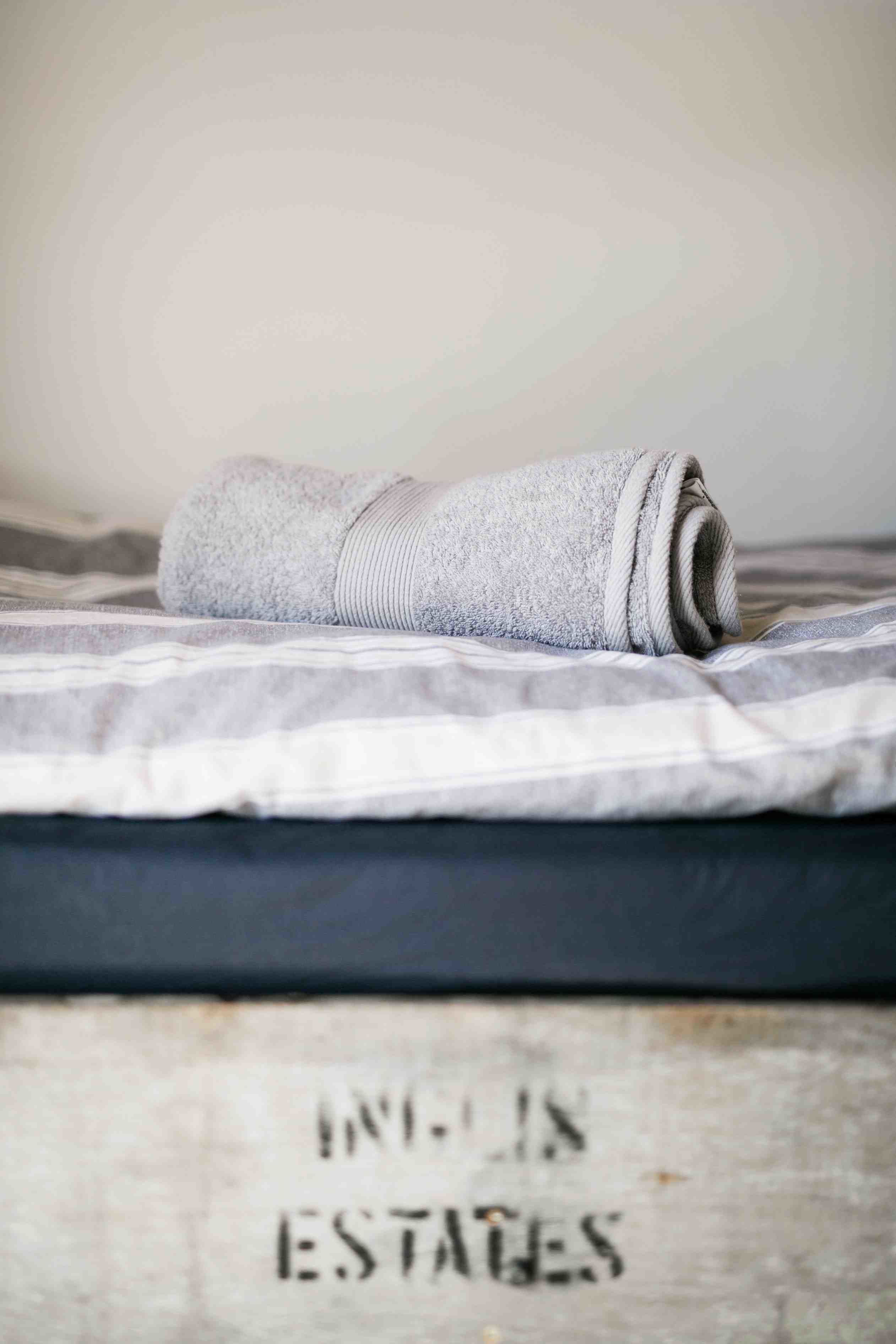 A rolled towel on a bed with a striped blanket.