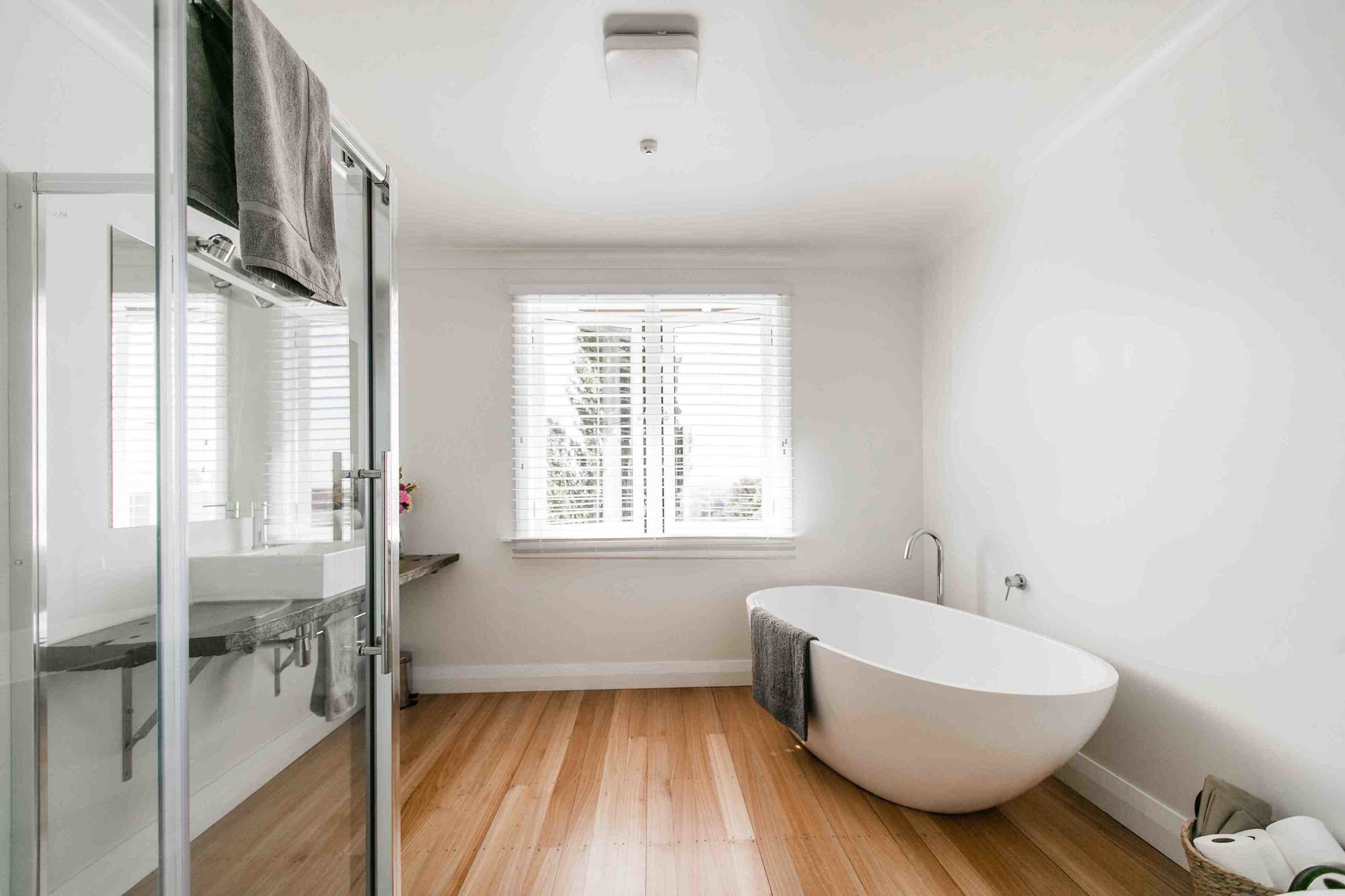 A modern bathroom with a freestanding bathtub, a glass shower enclosure, and a window with blinds.