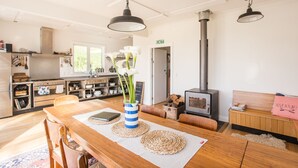 Una cocina moderna con comedor, estufa de leña y un rincón acogedor con estantería y un cartel rosa.