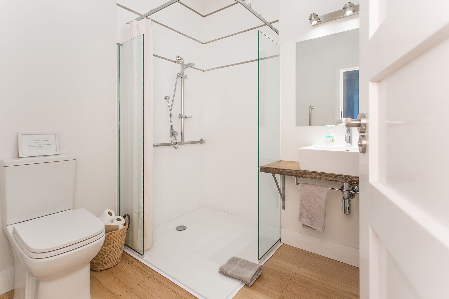 Un baño moderno con cabina de ducha de vidrio, inodoro blanco, lavamanos con encimera de madera y espejo sobre el lavamanos.