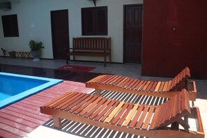 A pool area with two wooden lounge chairs and a bench. - Pousada Vital (Jijoca de Jericoacoara)