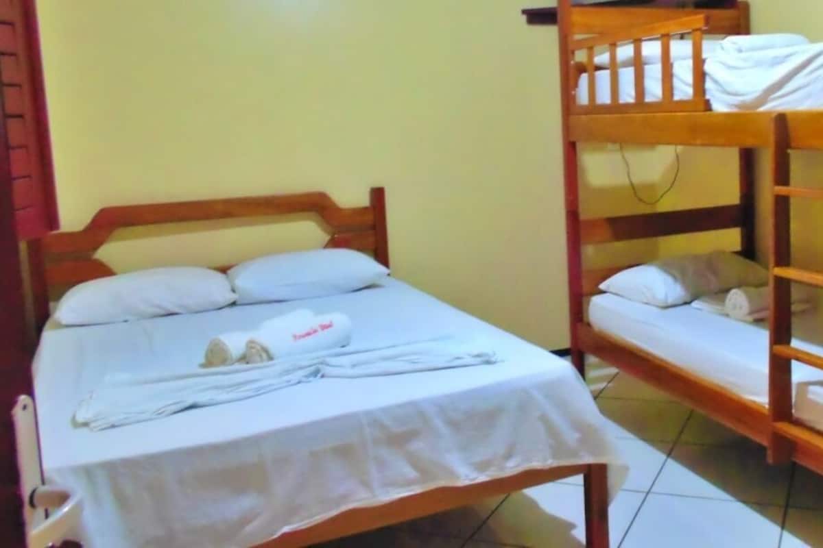 Una habitación con dos literas de madera, una con la cama inferior y otra con la superior. Hay una pequeña mesa con mantel blanco y una toalla encima.