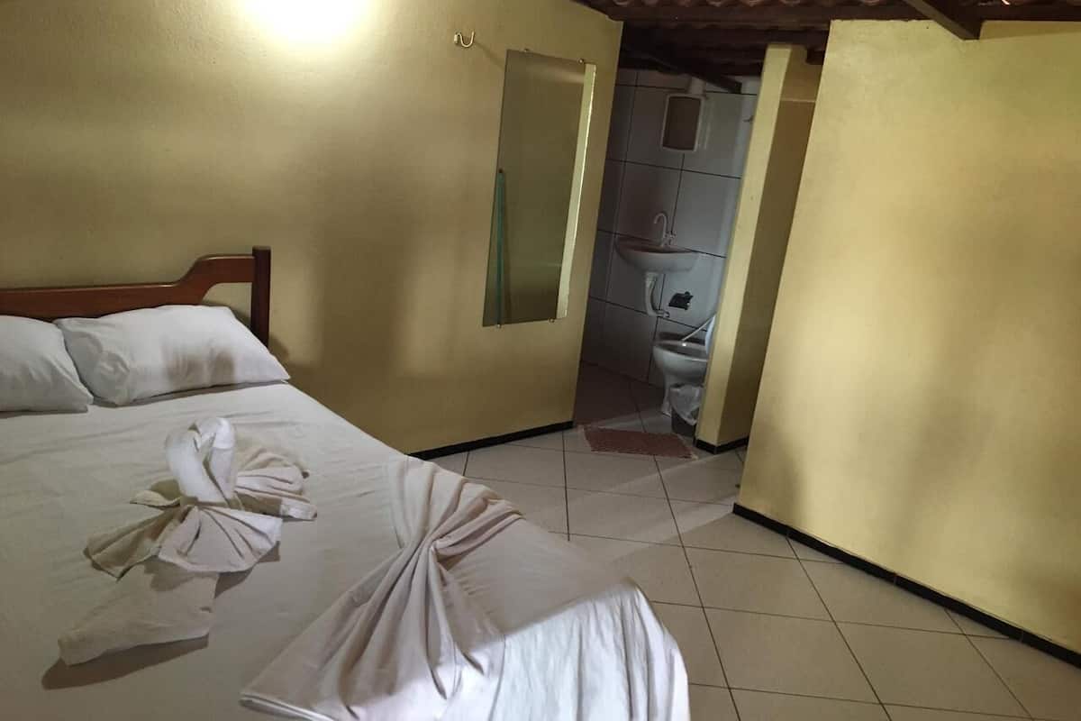 Habitación de hotel con cama, una mesita con toallas, un espejo y baño visible a través de una puerta abierta.