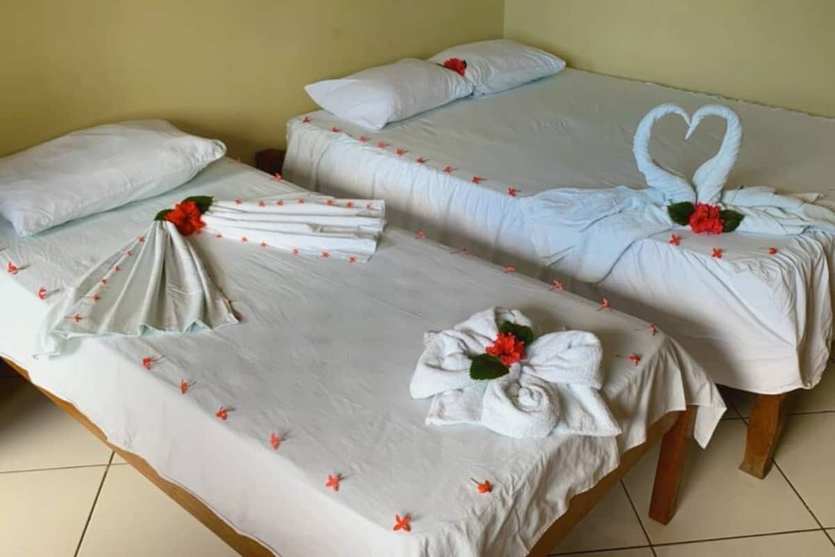 Habitación de hotel con dos camas, cada una decorada con toallas dobladas, flores rojas y una decoración de cisne con forma de corazón.