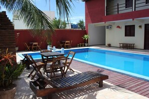 Una piscina con sillas de descanso y una mesa, rodeada de macetas con plantas y un muro rojo.