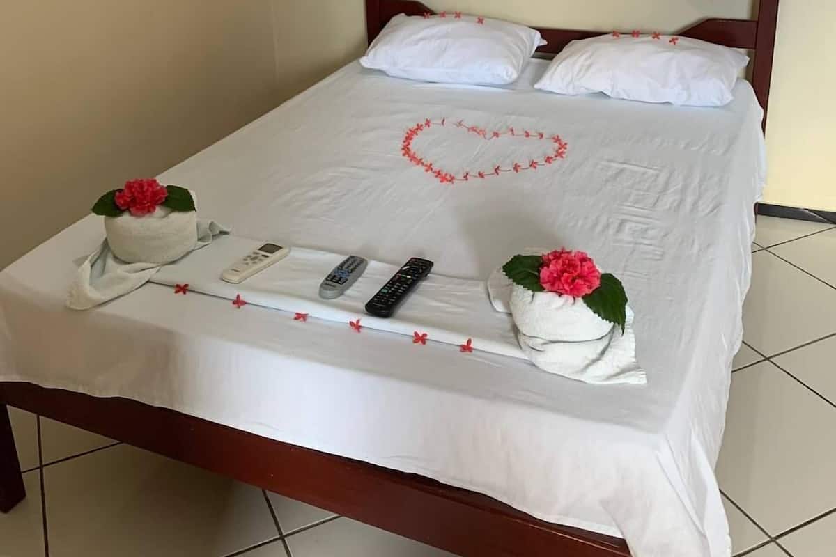 Una cama bien hecha con sábanas blancas, un adorno con forma de corazón en la colcha y dos almohadas decorativas con flores.