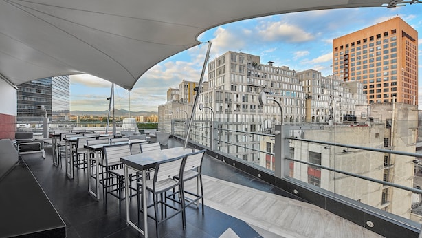 A rooftop terrace with tables and chairs, offering a view of the cityscape.