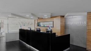 A modern hotel reception area with a black reception desk, a wooden accent wall, and a sign for CityExpress Hotels.