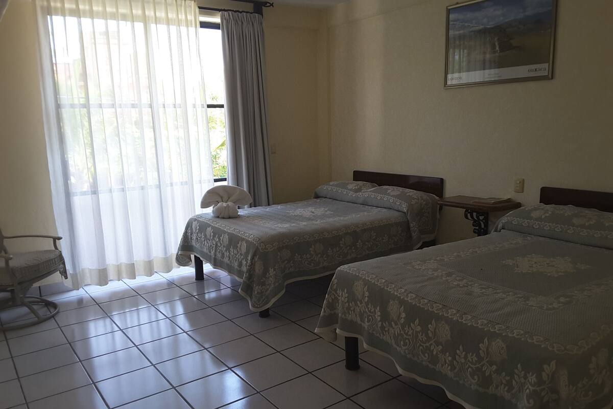 Une chambre d’hôtel avec deux lits, une chaise, une petite table et une fenêtre avec des rideaux.