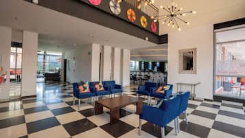 A lobby with checkered flooring, blue seating, a wooden coffee table, and a ceiling light fixture.