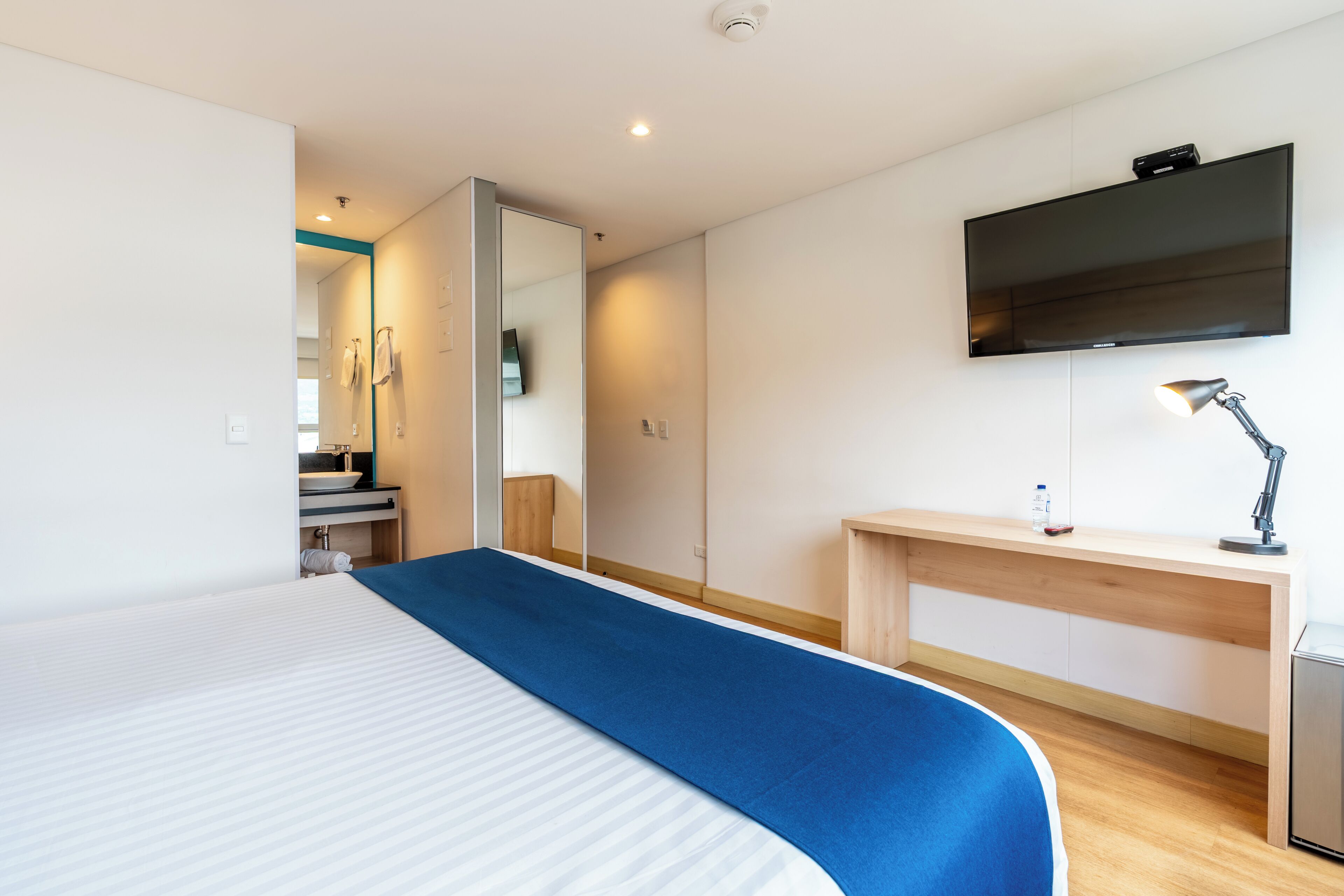 A hotel room with a large bed, a desk, a TV mounted on the wall, and a mirror.