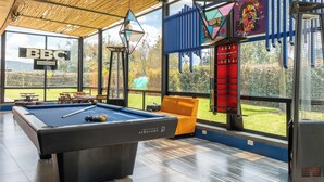 Een pooltafel in een ruimte met grote ramen, een bord met de tekst 'BBC CERVEERIA' en uitzicht op groen buiten.